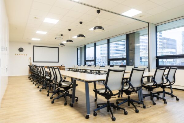 Moderne vergaderruimte aan de Hoogoorddreef met lange tafels, bureaustoelen en grote ramen met uitzicht op kantoorgebouwen.