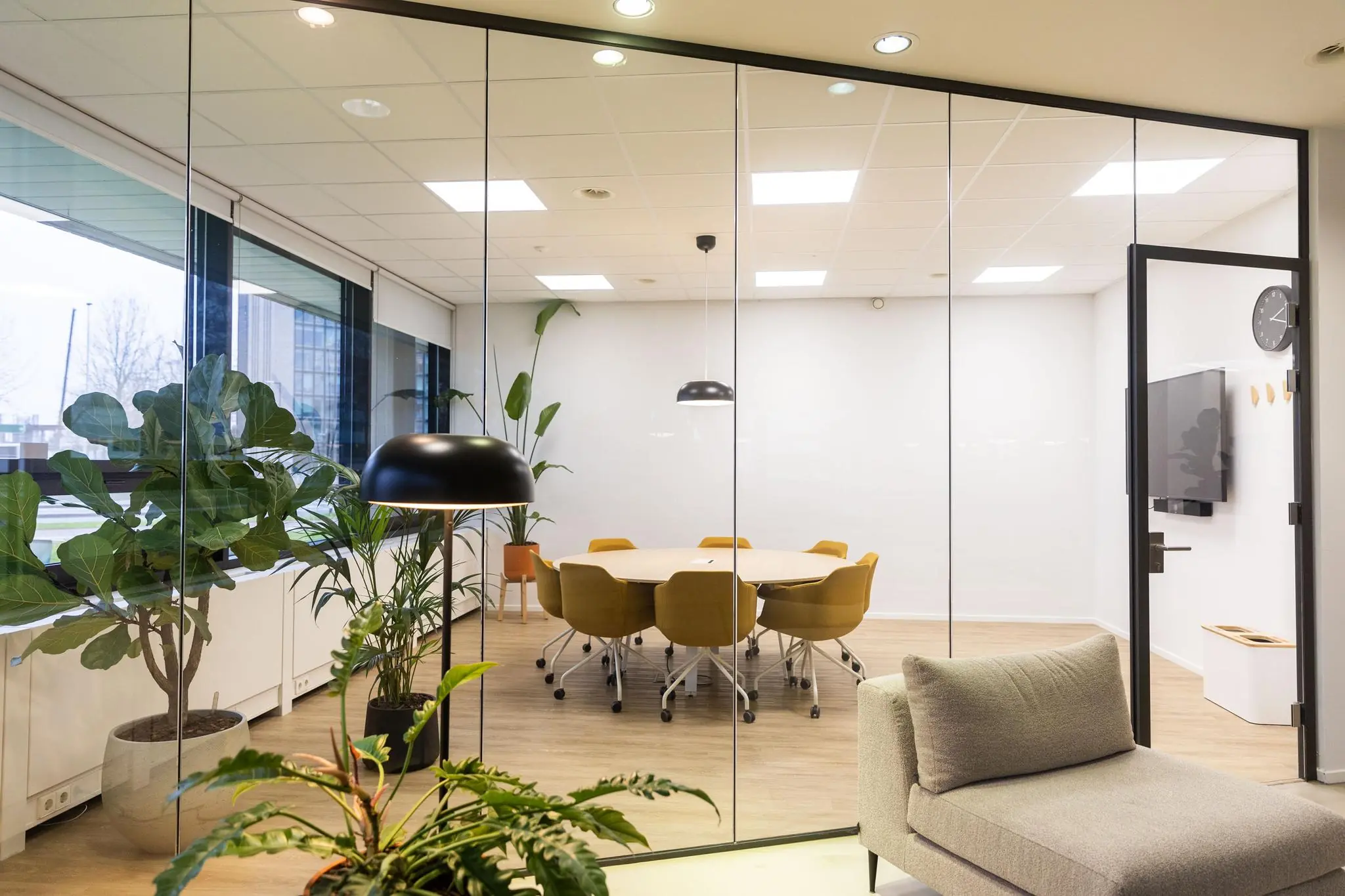 Moderne vergaderruimte aan de Hoogoorddreef met grote glazen wanden, gele stoelen en omringende planten.