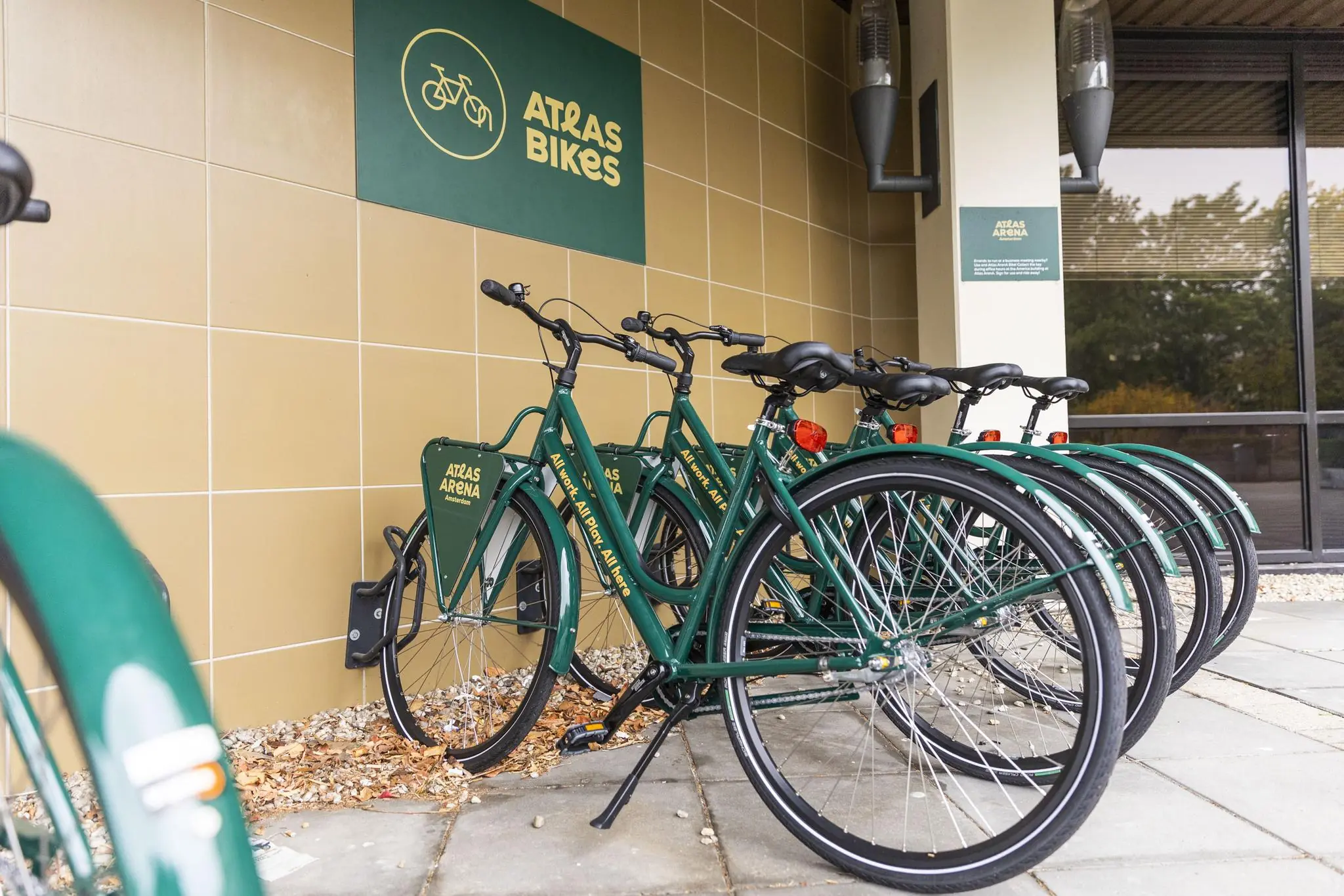 Groene deelfietsen van ATRAS Bikes staan opgesteld bij het ATRAS Arena gebouw aan de Hoogoorddreef.