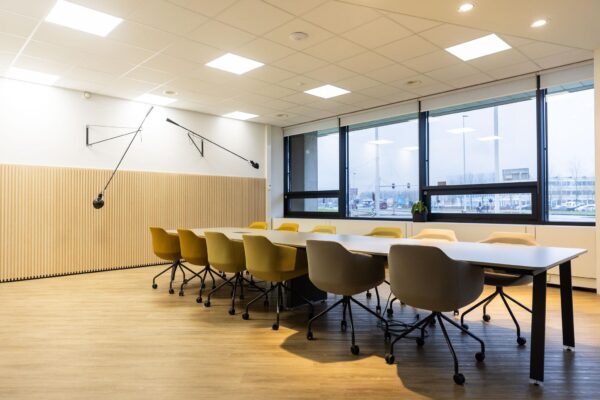 Moderne vergaderruimte aan de Hoogoorddreef met lange tafel, gele en beige stoelen en grote ramen met uitzicht op de straat.