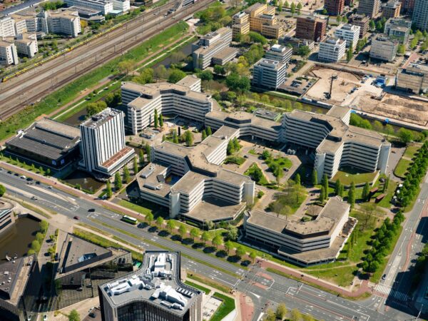 Luchtfoto van het kantoorgebouwcomplex aan de Hoogoorddreef in Amsterdam-Zuidoost, omringd door wegen, spoorlijnen en andere stedelijke bebouwing.