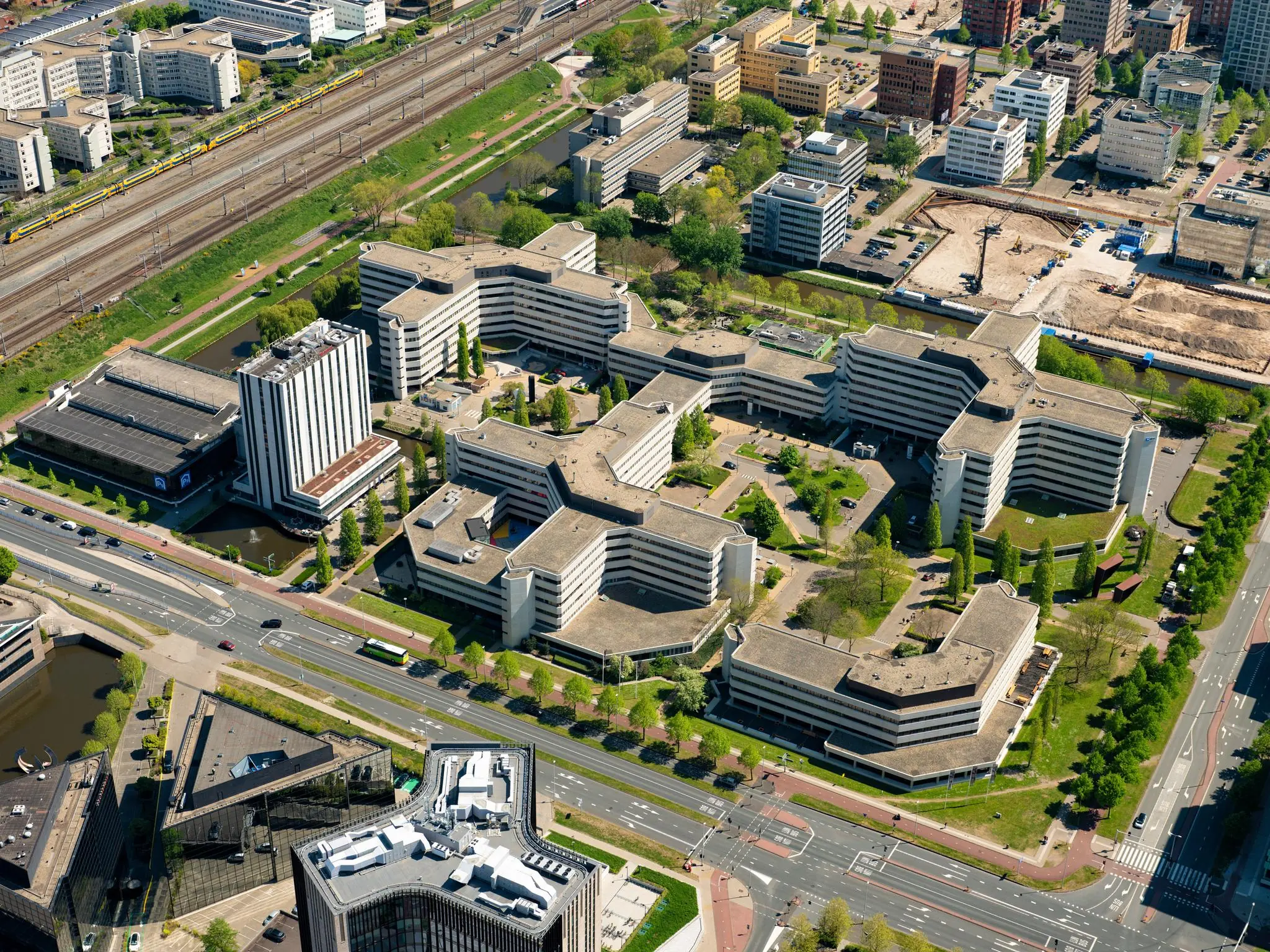 Luchtfoto van het kantoorgebouwcomplex aan de Hoogoorddreef in Amsterdam-Zuidoost, omringd door wegen, spoorlijnen en andere stedelijke bebouwing.