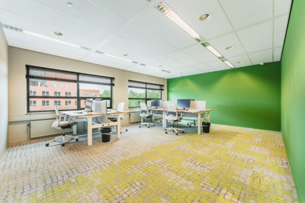 Een moderne, lichte kantoorruimte met witte bureaus, stoelen en groene muren.
