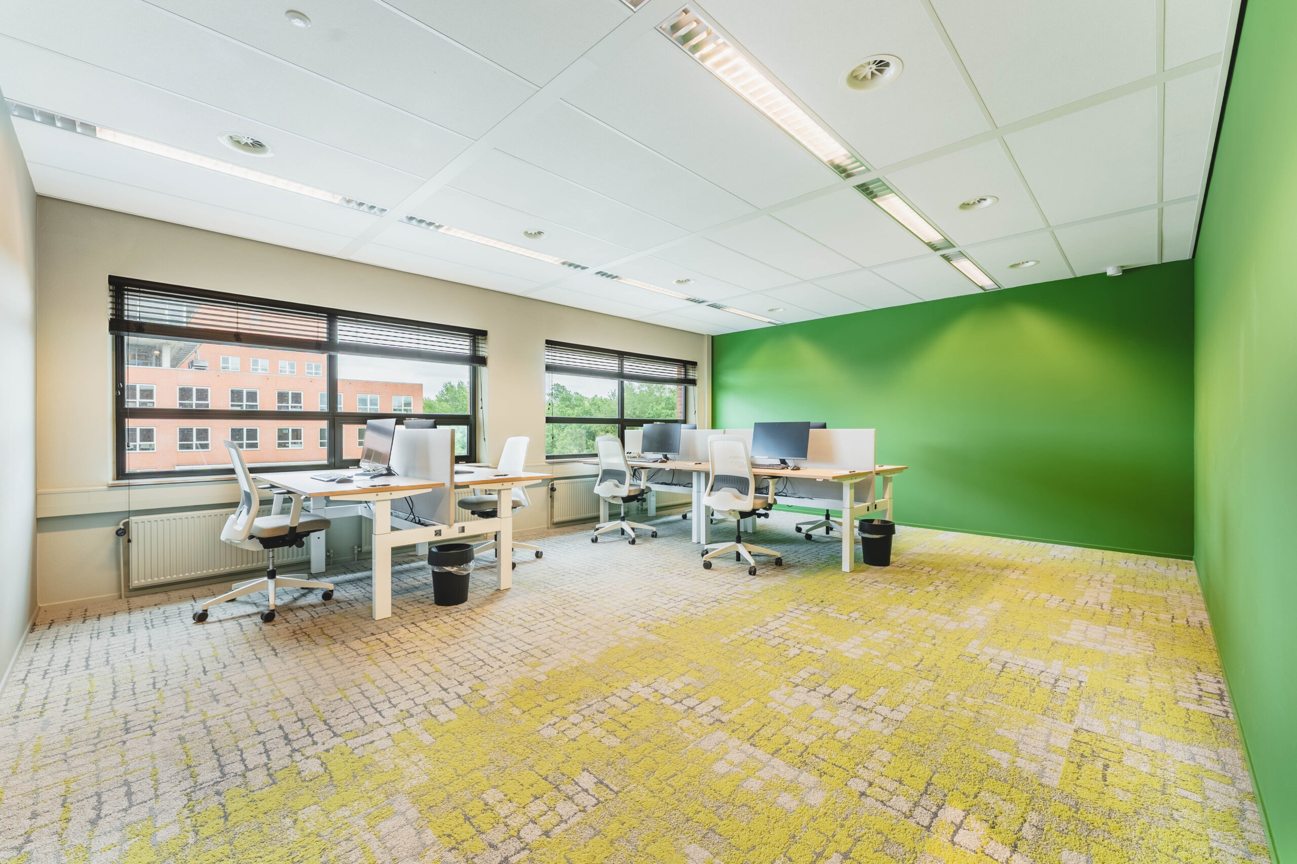 Een moderne, lichte kantoorruimte met witte bureaus, stoelen en groene muren.