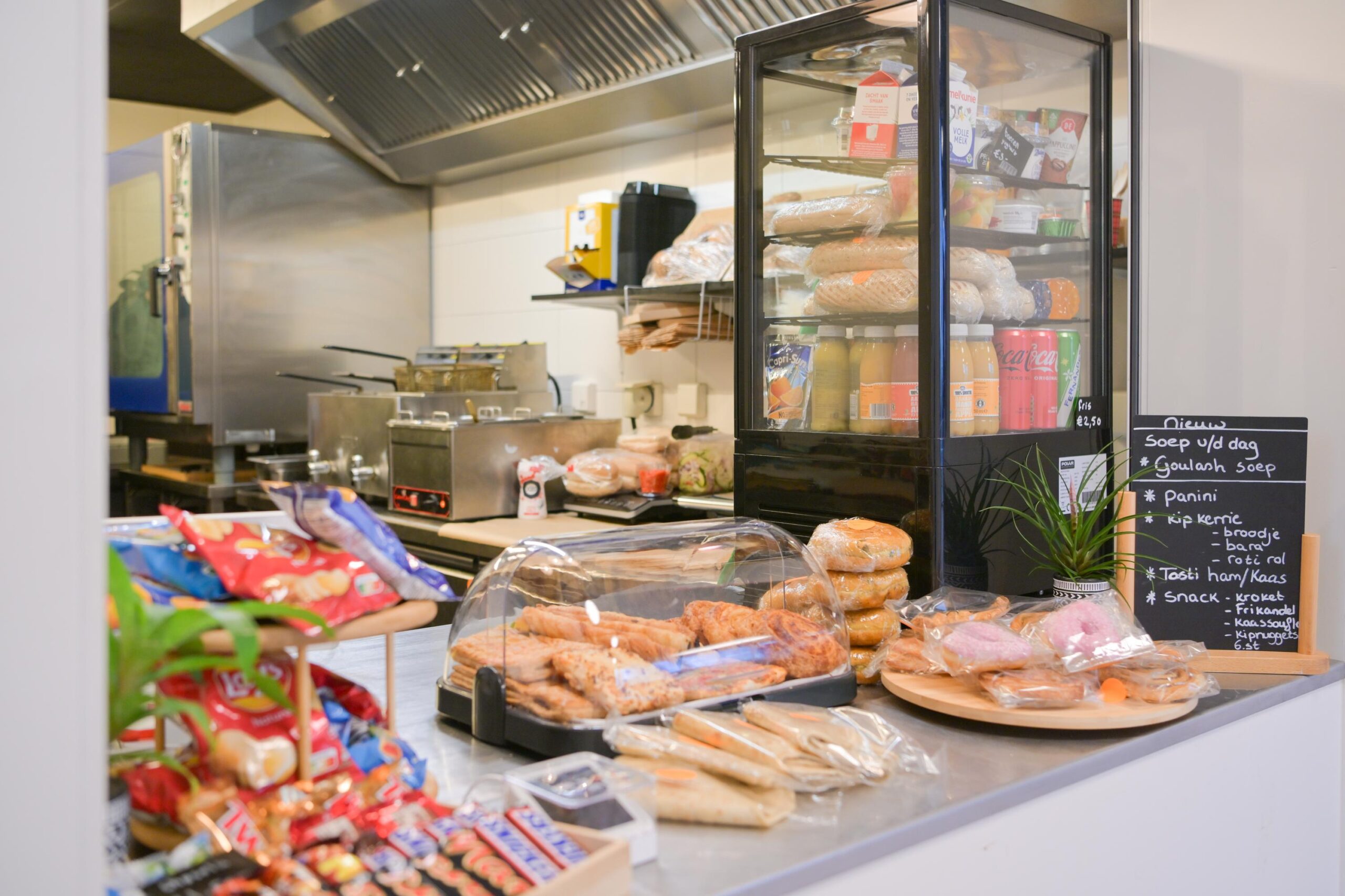 Een keukenaanrecht in een café met verschillende snacks, verpakte broodjes en een krijtbord met het menu.