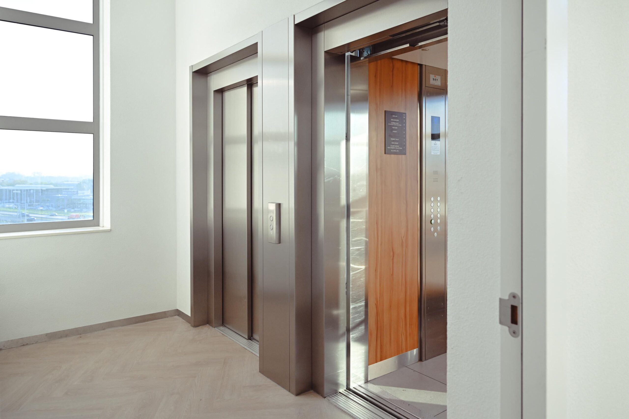 Een moderne lift met open deuren in een gebouw, met zicht op een groot raam.