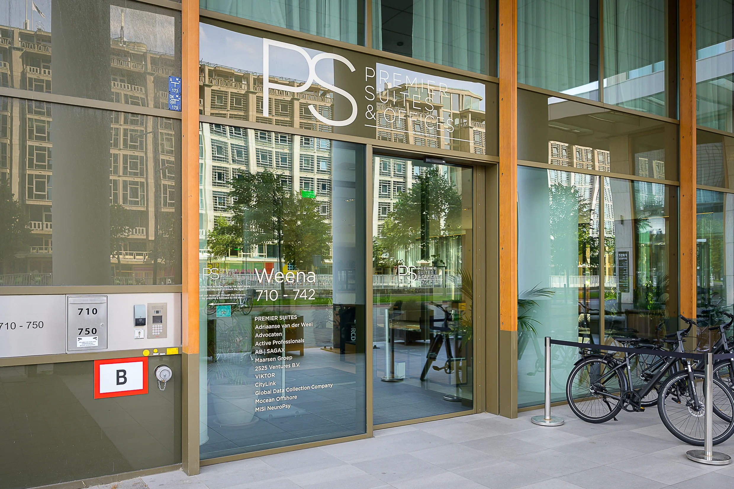 Entrance to the Premier Suites office building at Weena 710–742 with glass doors and parked bicycles in front.