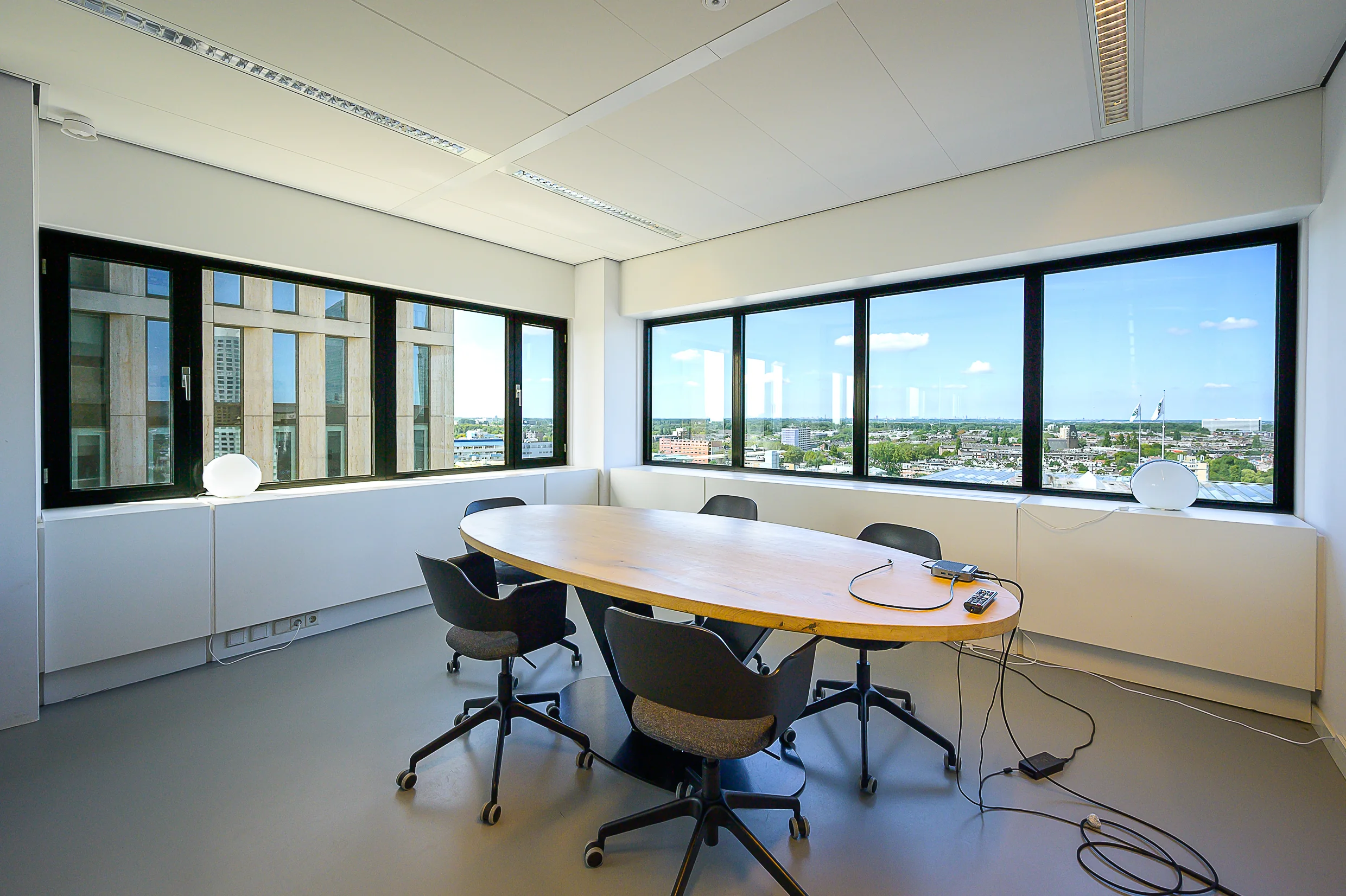 Modern conference room at Weena 210, featuring a large oval table, office chairs, and panoramic city views through large windows.