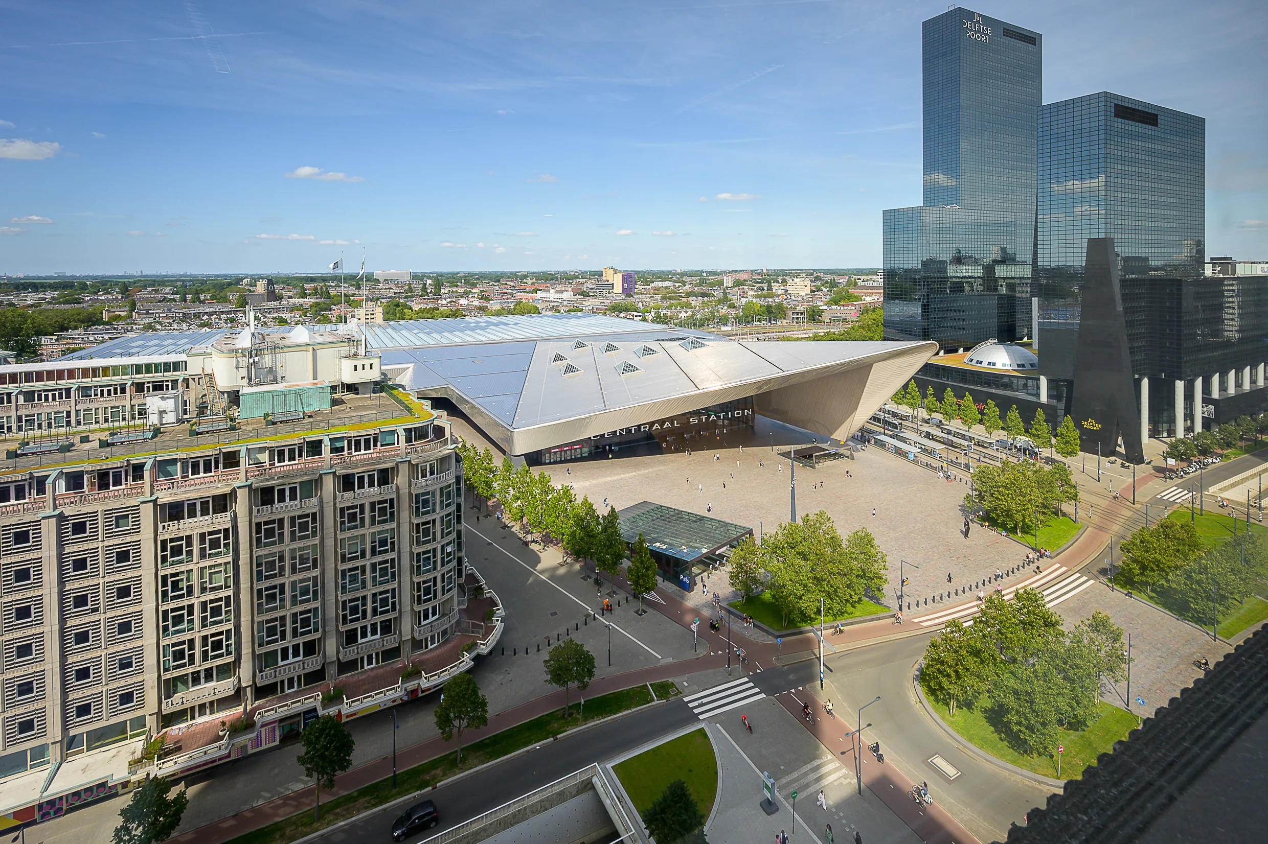 Aerial view of Rotterdam Central Station with surrounding modern buildings and busy streets on a sunny day.