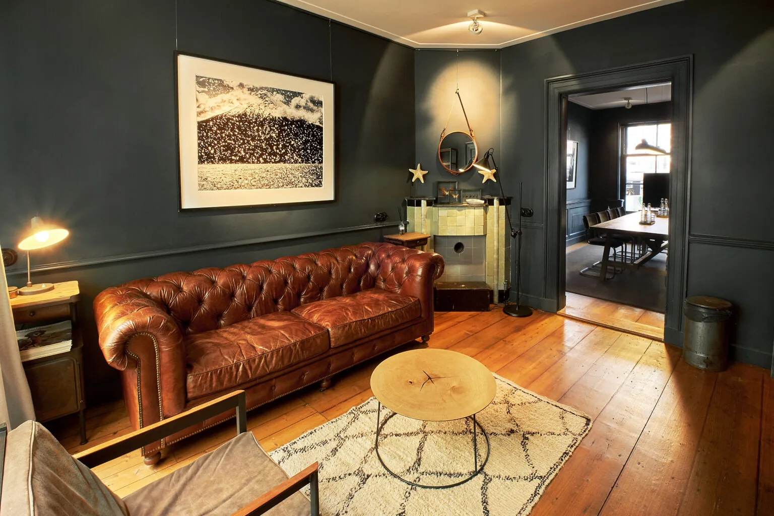 Stijlvol ingerichte woonkamer met een bruine leren chesterfieldbank, houten vloer en donkere muren aan de Singel.