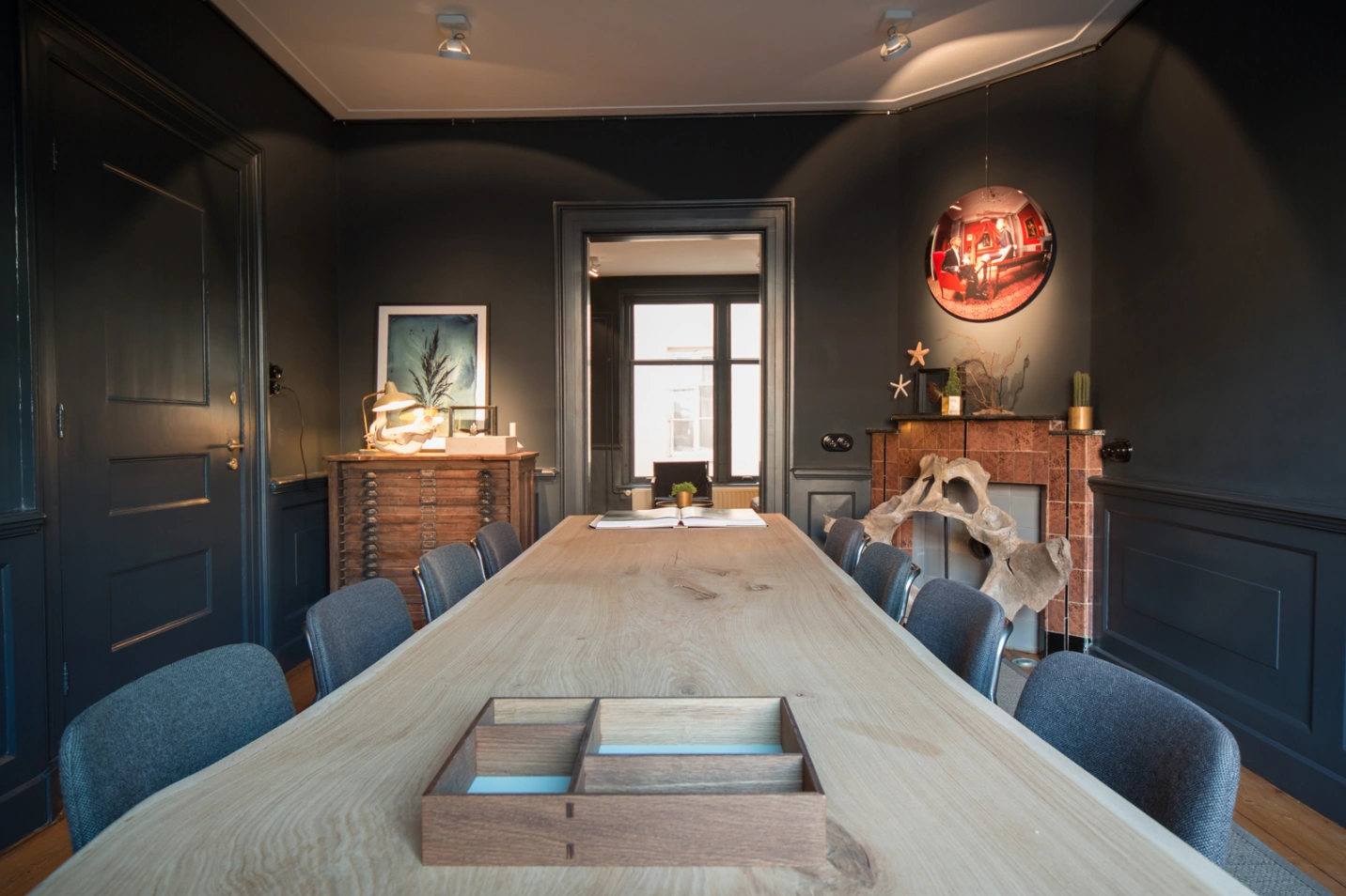 Moderne vergaderruimte aan de Singel met een lange houten tafel, donkerblauwe muren en kunstzinnige decoratie.