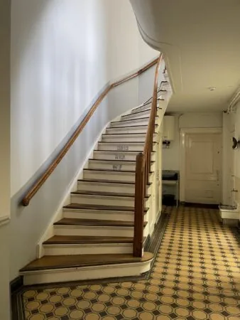 Trapopgang met houten leuning en betegelde vloer in een historisch gebouw aan de Singel.