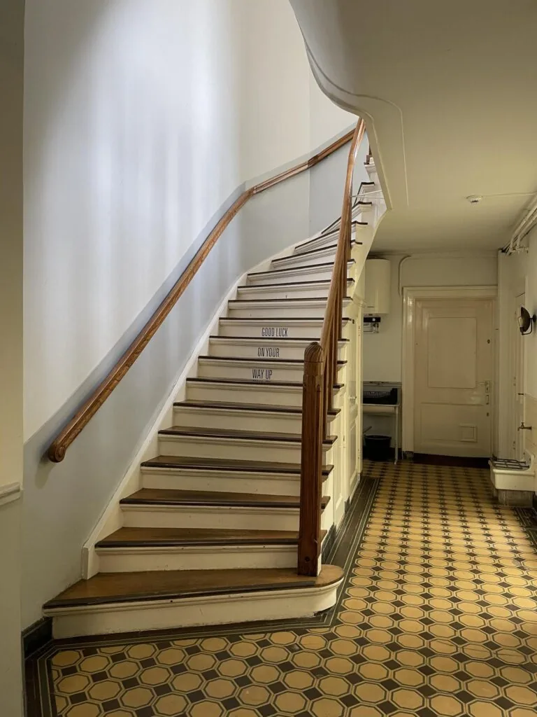 Trapopgang met houten leuning en betegelde vloer in een historisch gebouw aan de Singel.