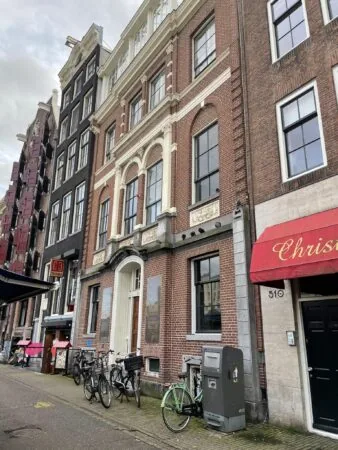 Gevel van klassieke panden aan de Singel in Amsterdam met fietsen en een rode luifel op de voorgrond.