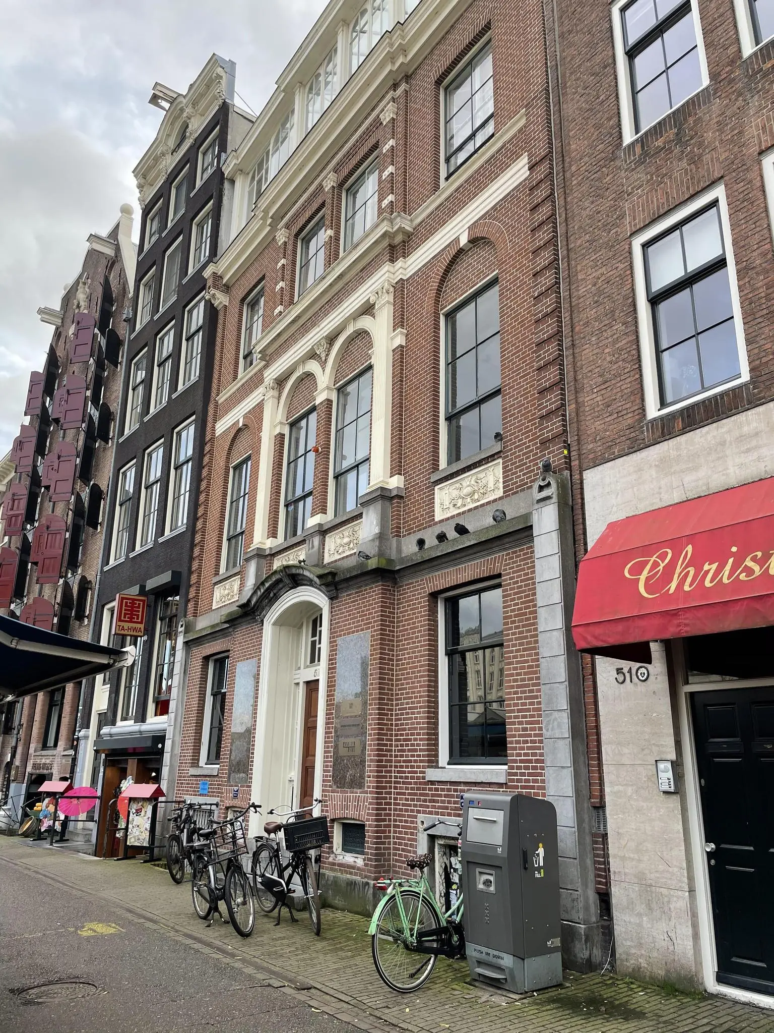 Gevel van klassieke panden aan de Singel in Amsterdam met fietsen en een rode luifel op de voorgrond.