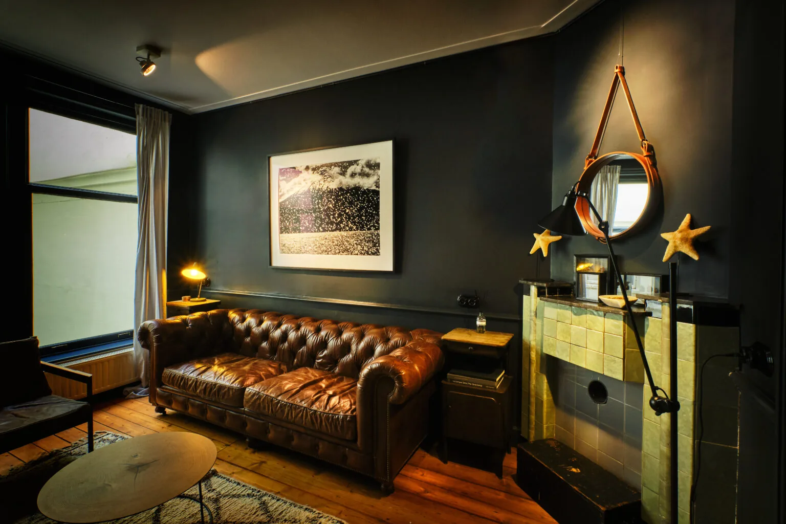 Stijlvol ingerichte woonkamer met een bruine leren chesterfieldbank, een open haard met spiegel en maritieme decoratie.