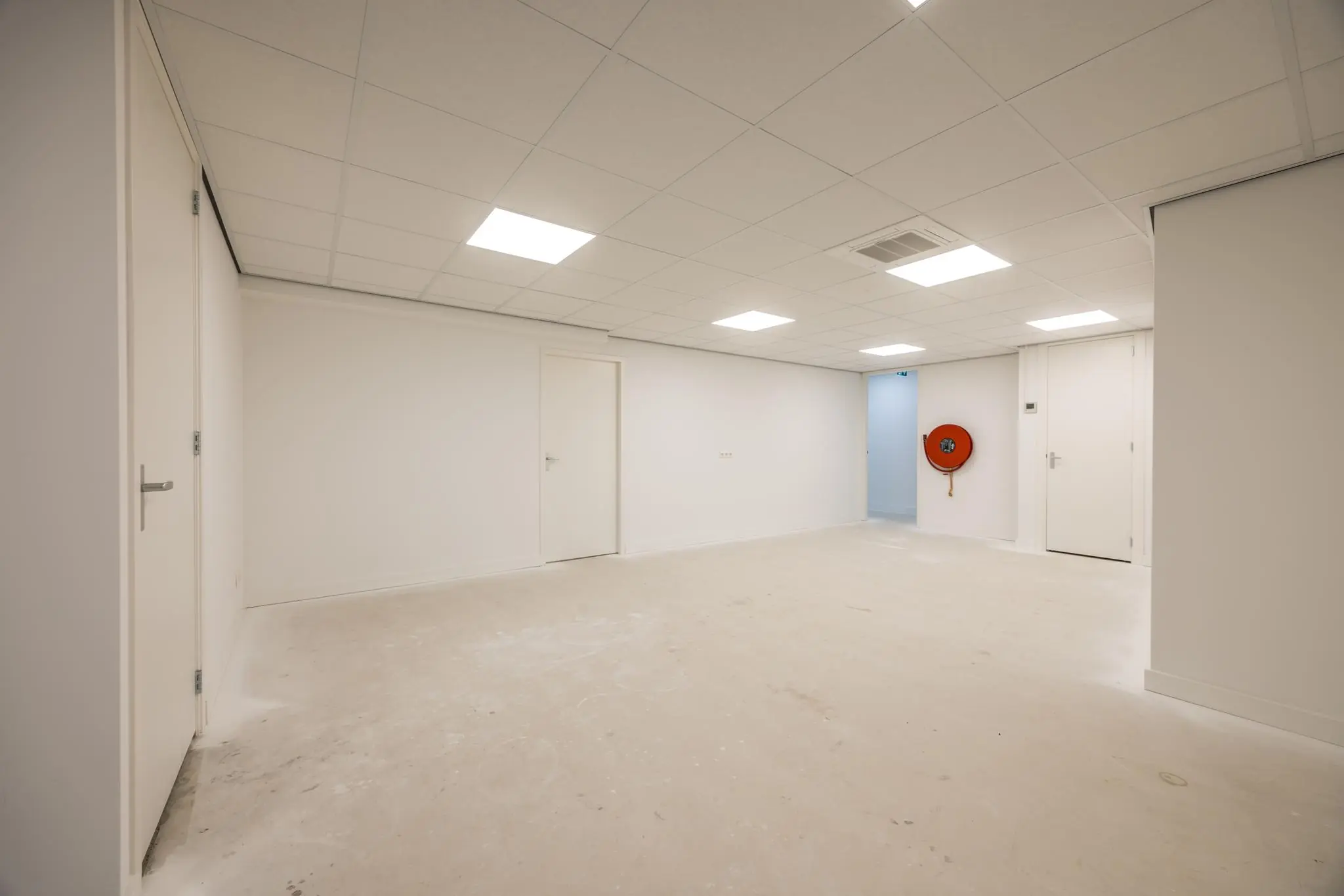 Lege, wit afgewerkte ruimte aan de Wallesteinlaan met systeemplafond, meerdere deuren en een oranje brandslanghaspel aan de muur.