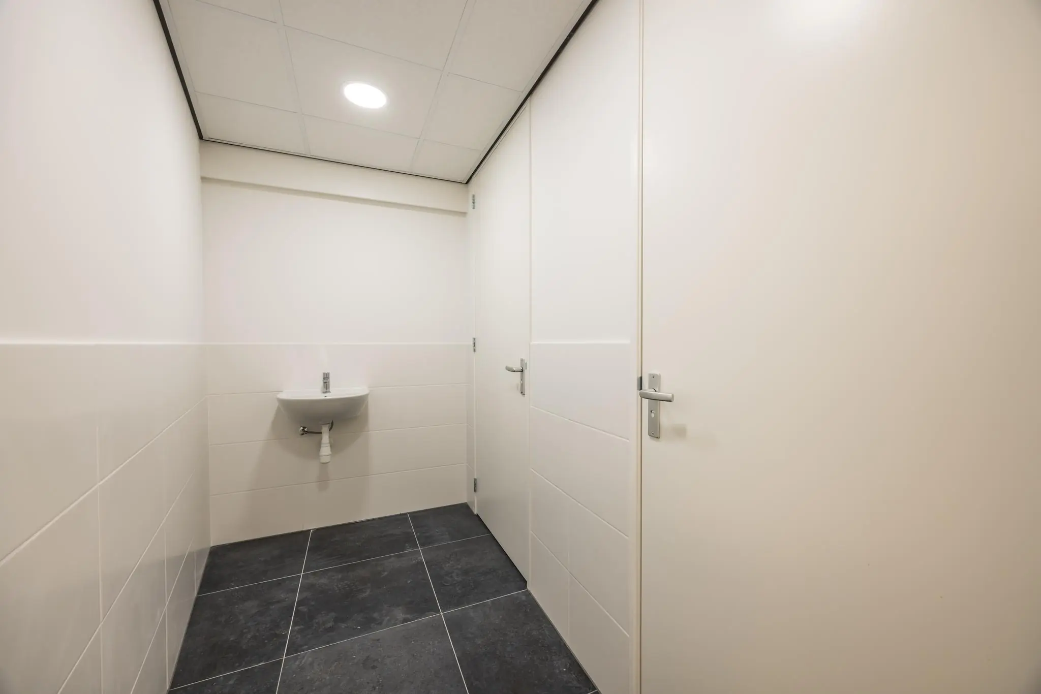 Nette, witte toiletruimte aan de Wallesteinlaan met een kleine wandwastafel en donkere vloertegels.