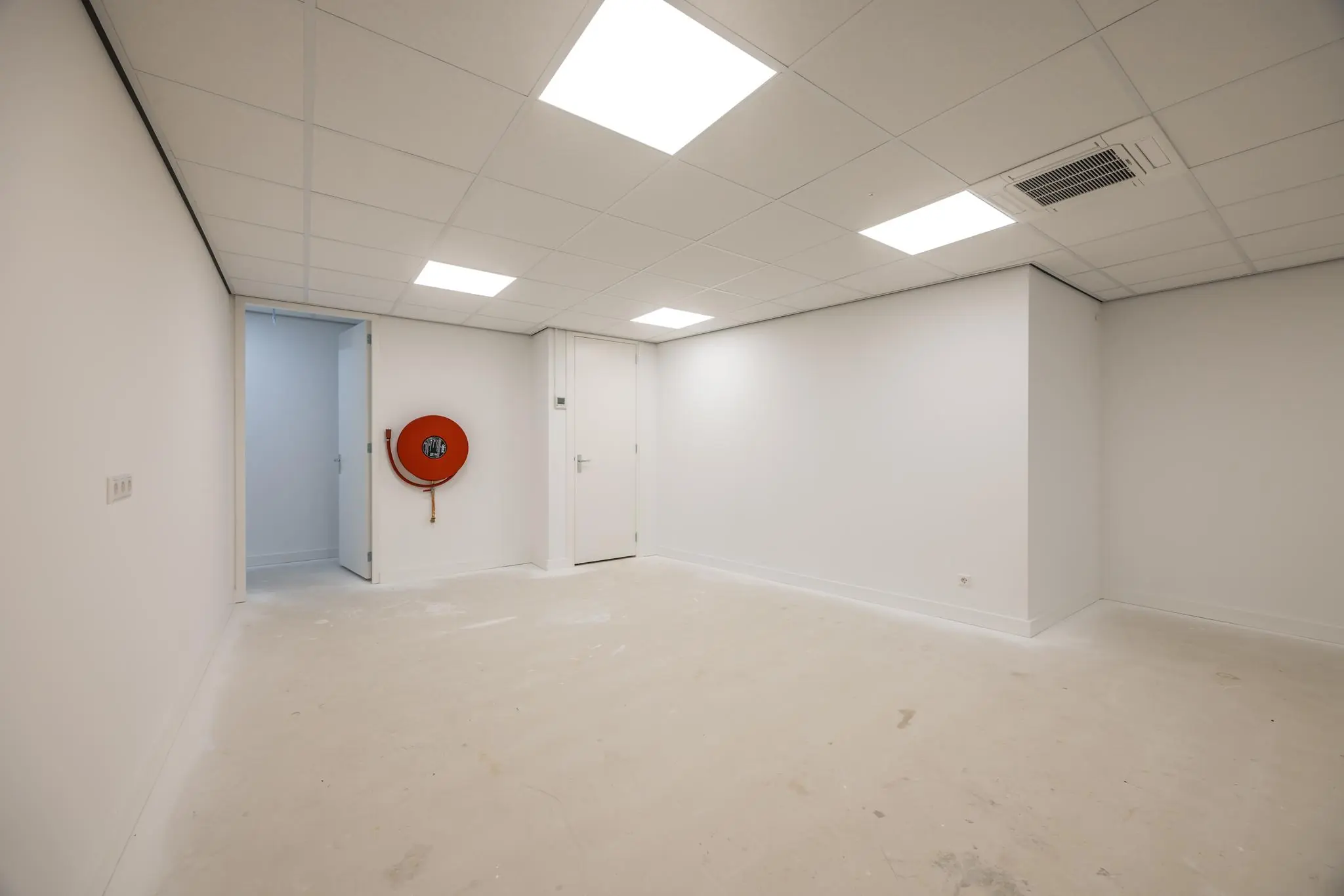 Lege, wit afgewerkte ruimte aan de Wallesteinlaan met systeemplafond, brandslanghaspel en twee gesloten deuren.