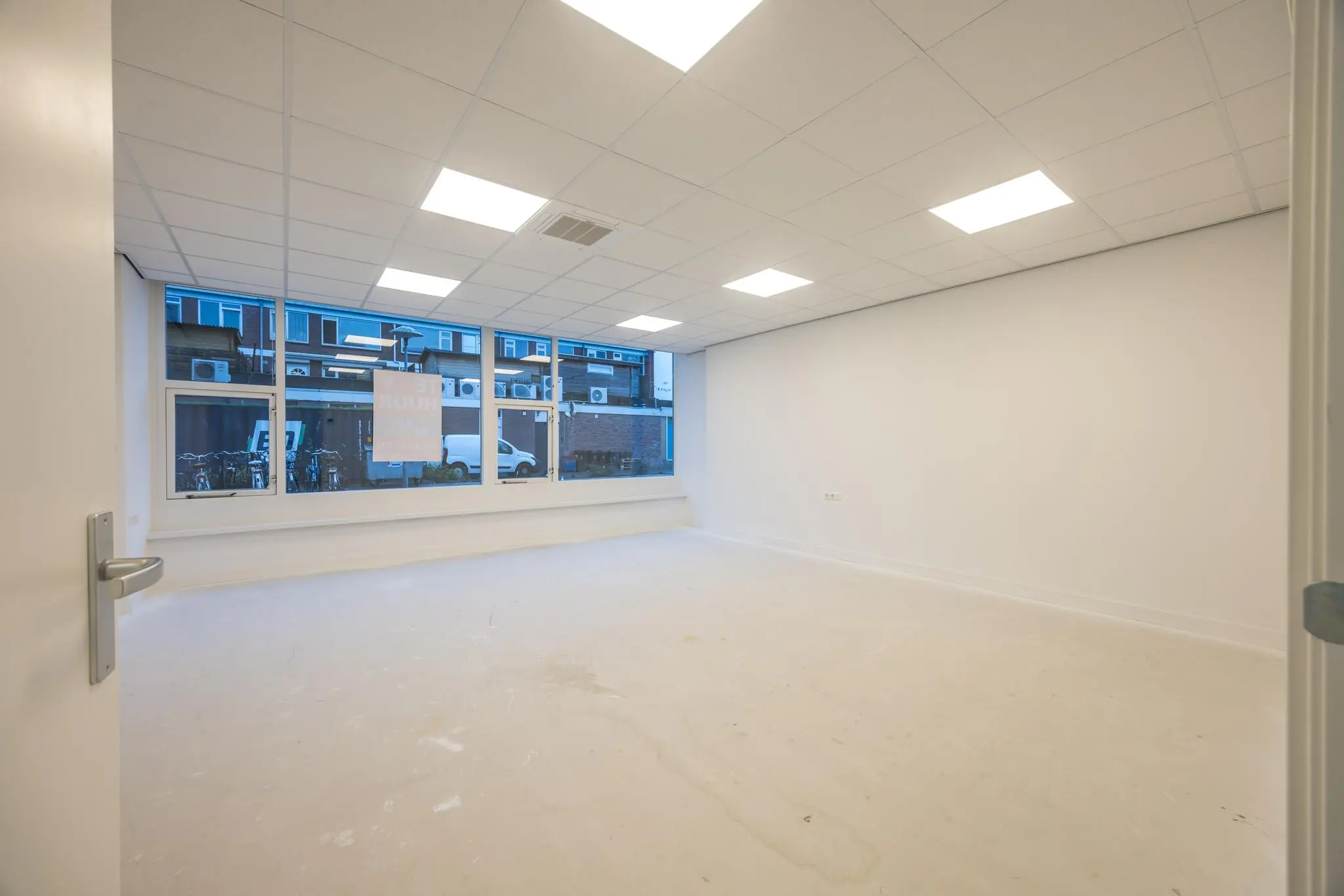 Leeg, wit afgewerkte kantoorruimte aan de Wallesteinlaan met grote ramen en systeemplafondverlichting.