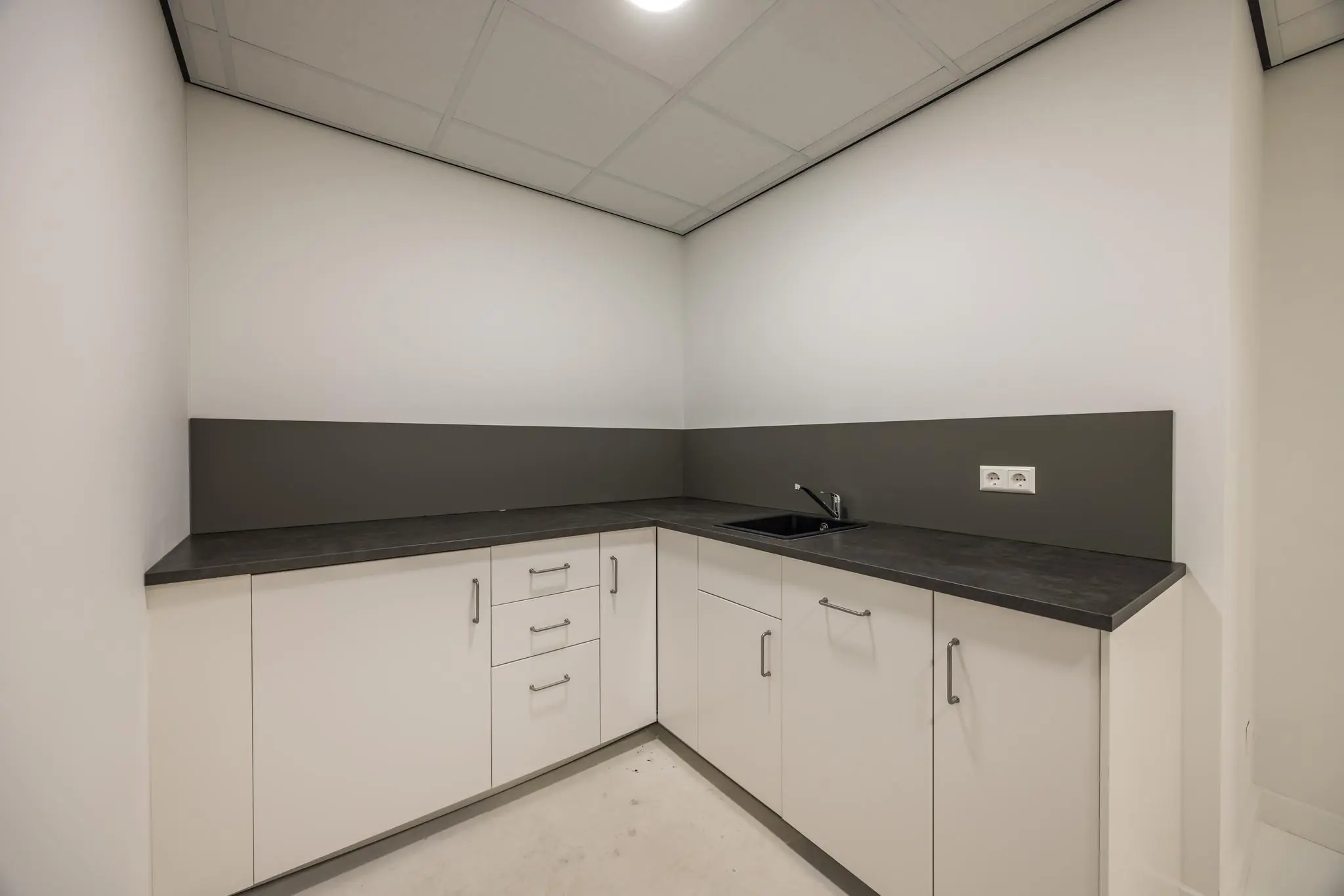 Moderne hoekkeuken met witte kasten, donker werkblad en ingebouwde spoelbak aan de Wallesteinlaan.