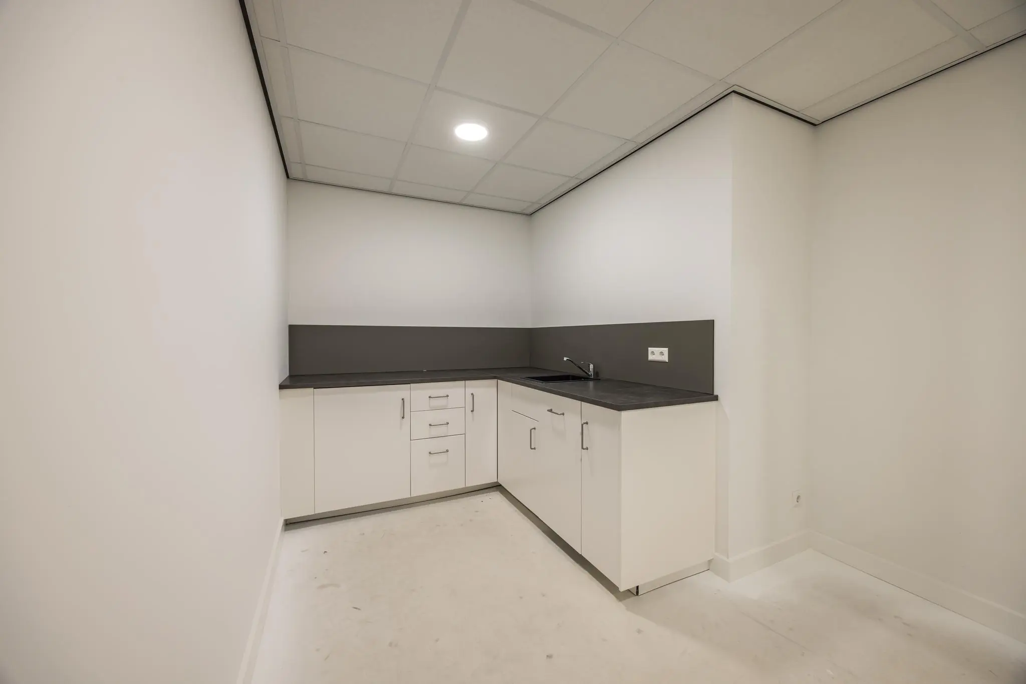 Moderne, witte hoekpantry met donker werkblad en inbouwspoelbak in een hoekruimte aan de Wallesteinlaan.