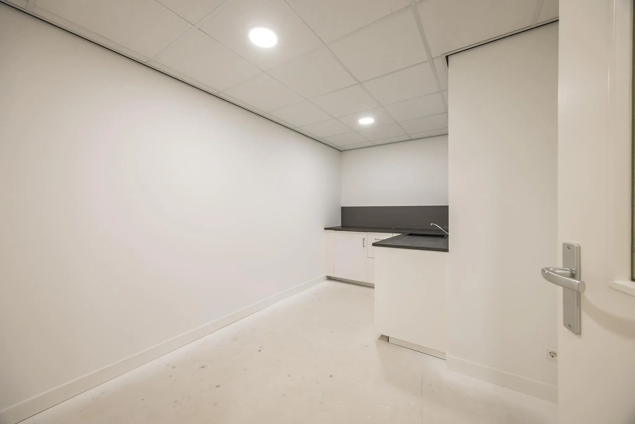 Kleine, strak afgewerkte pantry met witte kasten en donker aanrechtblad in een lege ruimte aan de Wallesteinlaan.