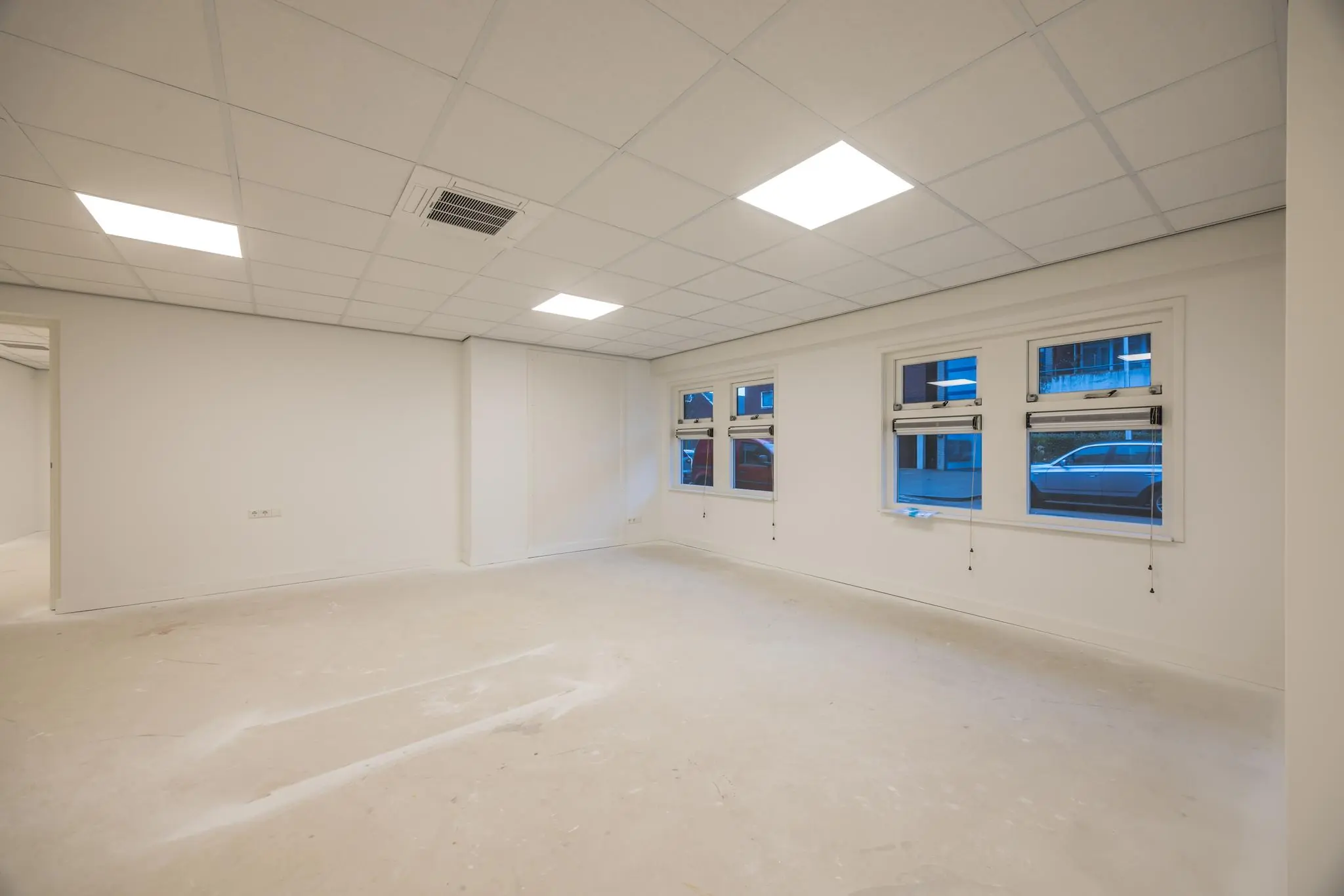 Leeg en witgeschilderd kantoor- of praktijkruimte aan de Wallesteinlaan met systeemplafond en ramen aan de straatzijde.
