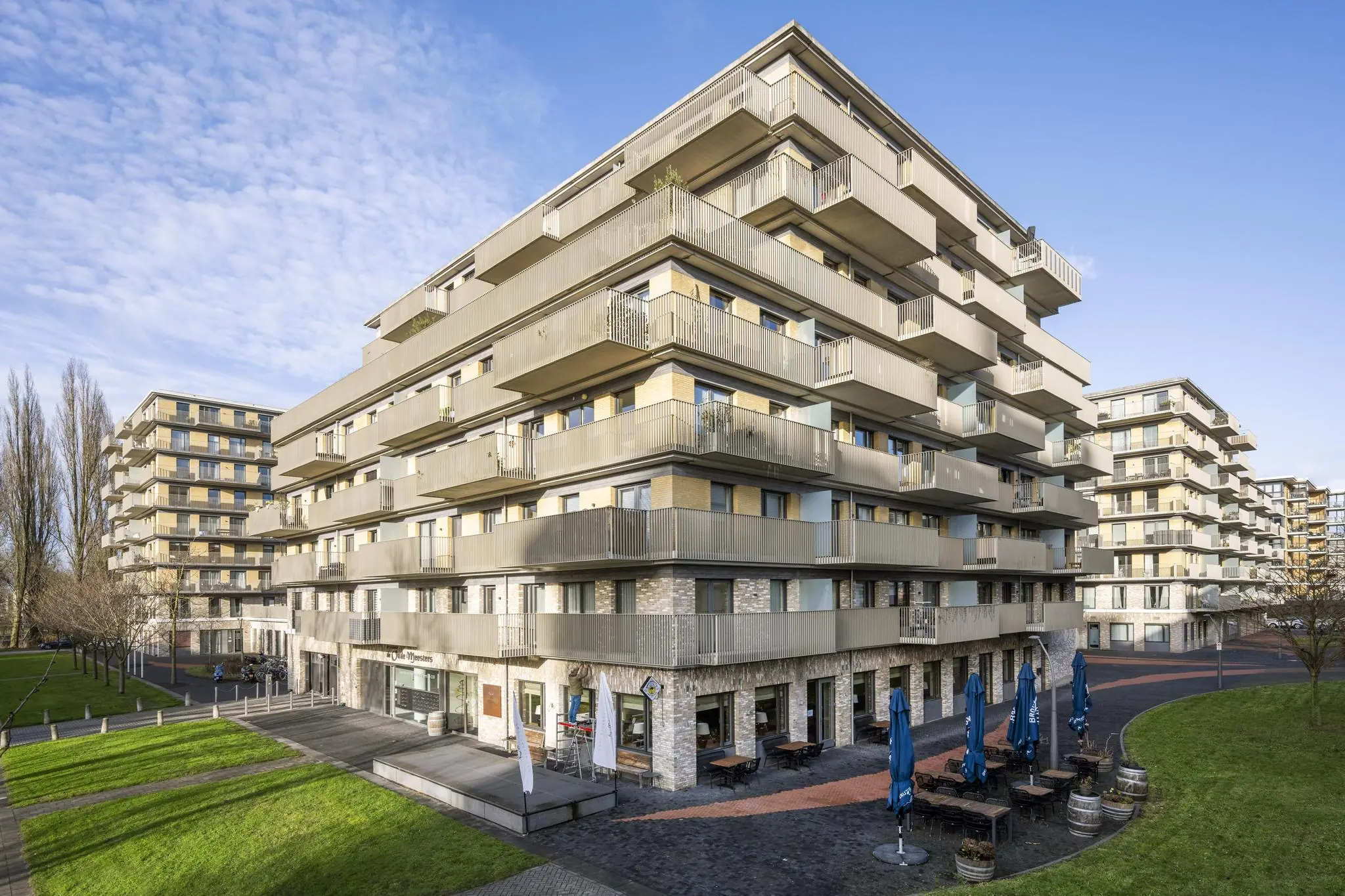 Moderne appartementencomplexen aan de Laan van de Helende Meesters met terrassen, groenstroken en horeca op de begane grond.