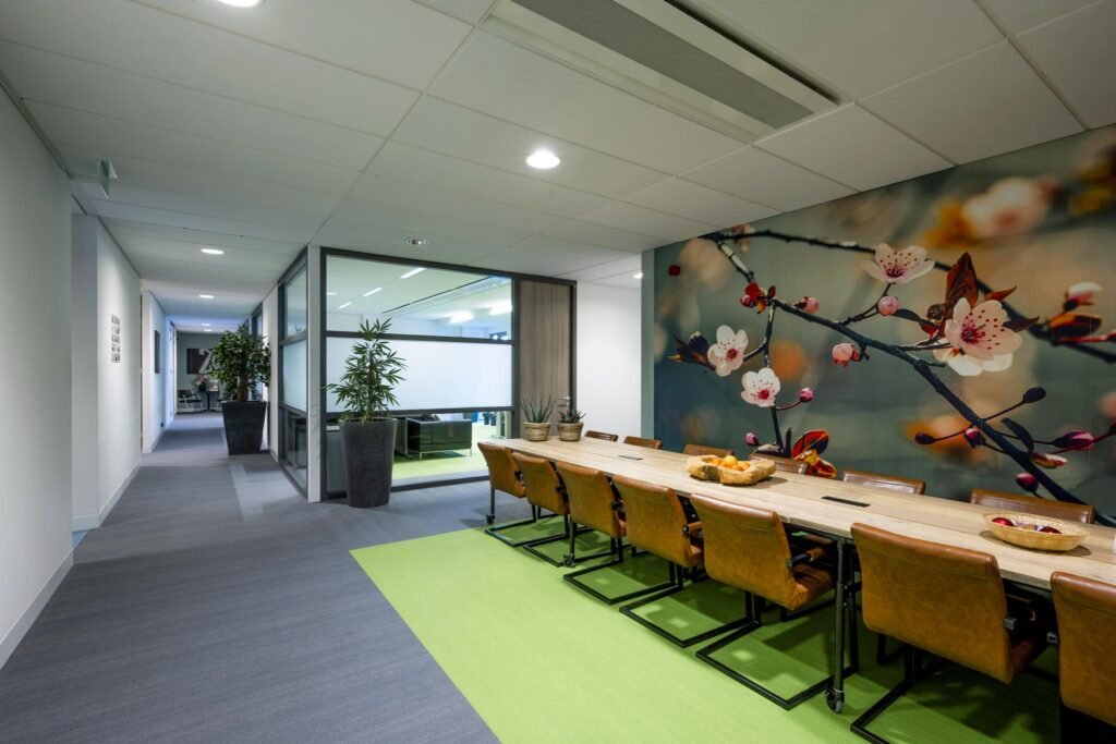 Vergaderruimte aan de Laan van de Helende Meesters met een lange houten tafel, leren stoelen en een grote wanddecoratie van bloesemtakken.
