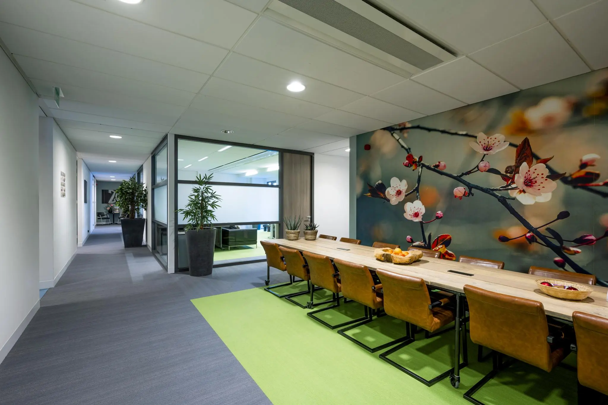Vergaderruimte aan de Laan van de Helende Meesters met een lange houten tafel, leren stoelen en een grote wanddecoratie van bloesemtakken.