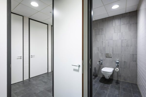 Modern openbaar toilet met grijze tegels en witte deuren aan de Laan van de Helende Meesters.