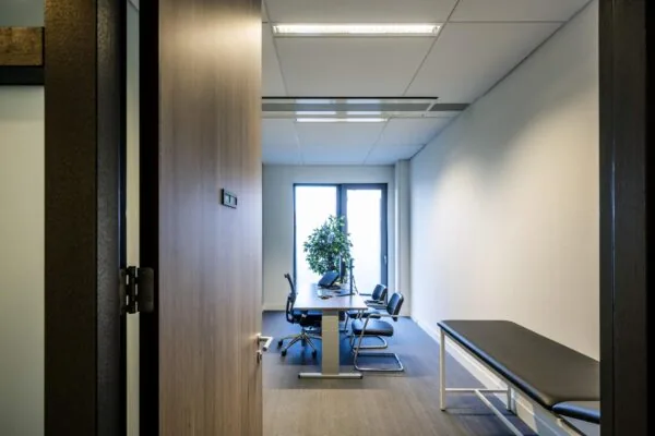 Moderne spreekkamer in een medisch centrum aan de Laan van de Helende Meesters met bureau, stoelen en onderzoeksbank.