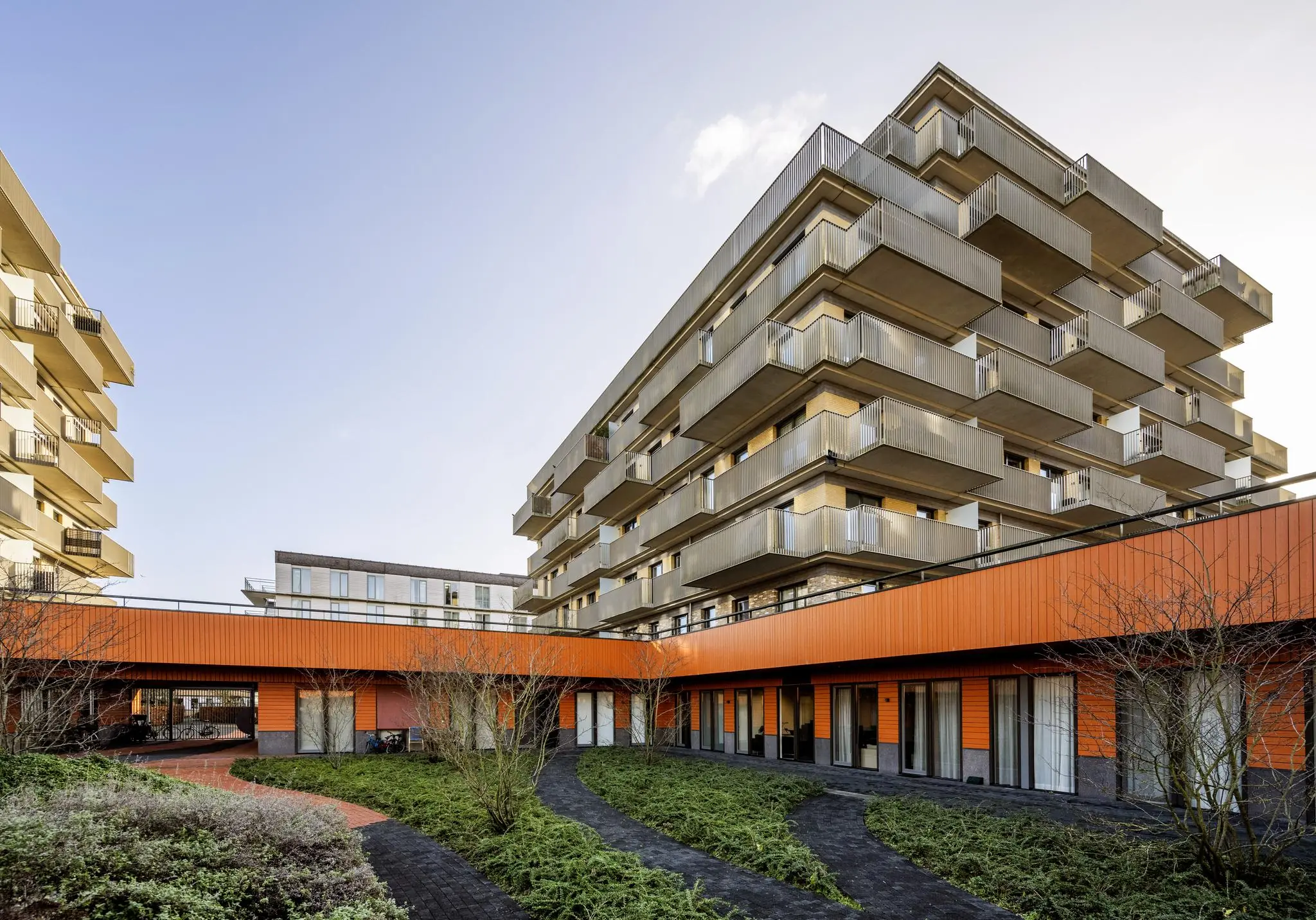 Moderne appartementencomplexen aan de Laan van de Helende Meesters met groene binnentuin en opvallende oranje gevel.