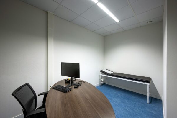 Onderzoeksruimte met bureau, computer en onderzoeksbank in een kliniek aan de Laan van de Helende Meesters.