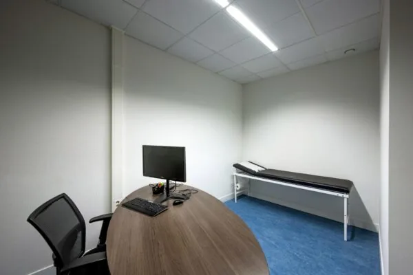 Onderzoeksruimte met bureau, computer en onderzoeksbank in een kliniek aan de Laan van de Helende Meesters.