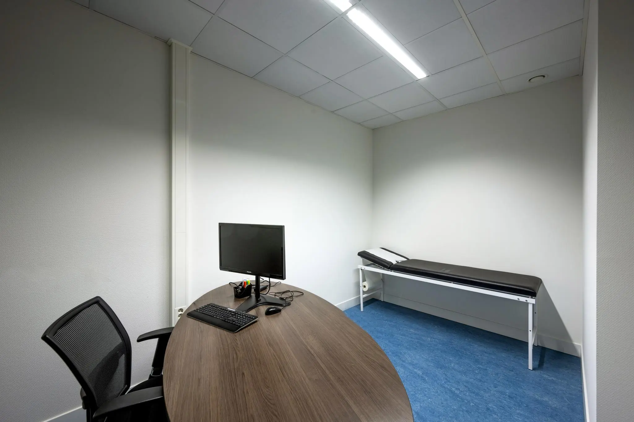 Onderzoeksruimte met bureau, computer en onderzoeksbank in een kliniek aan de Laan van de Helende Meesters.