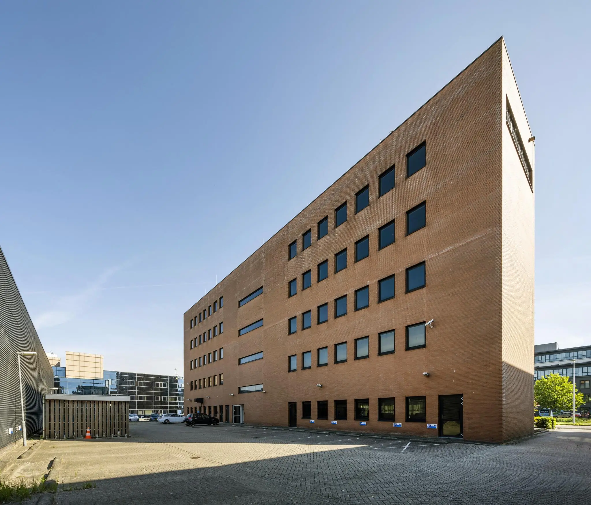 Bakstenen kantoorgebouw aan de Paasheuvelweg met meerdere verdiepingen en donkere raamkozijnen, gezien vanaf de parkeerplaats.