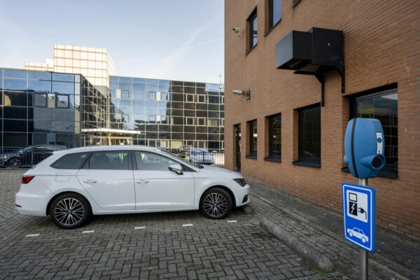 Witte auto geparkeerd naast een laadpaal bij een kantoorgebouw aan de Paasheuvelweg.