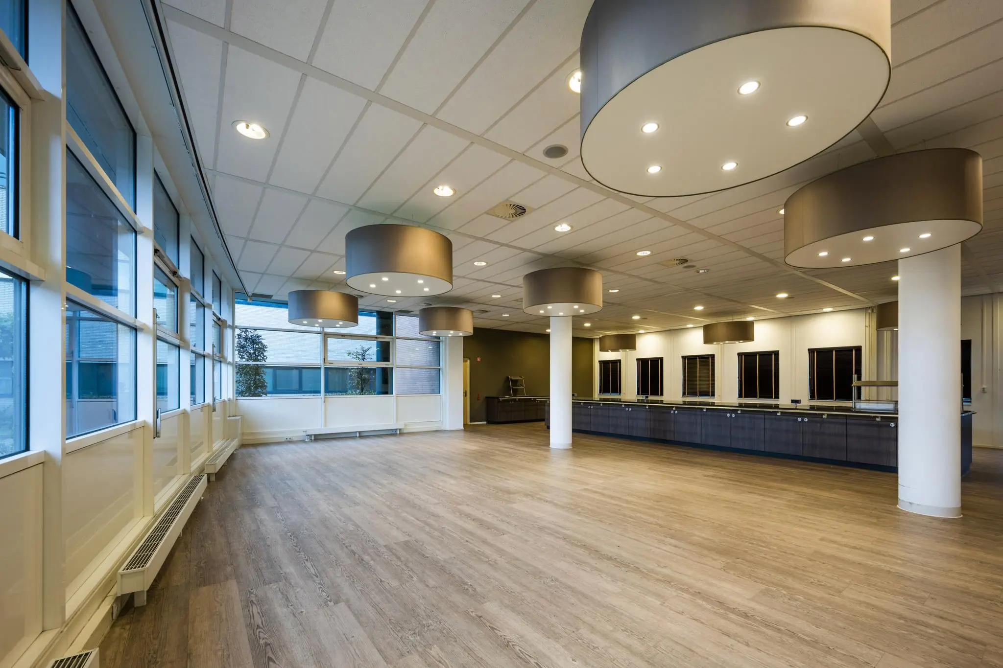 Ruime, moderne zaal aan de Paasheuvelweg met houten vloer, grote ramen en opvallende ronde plafondlampen.