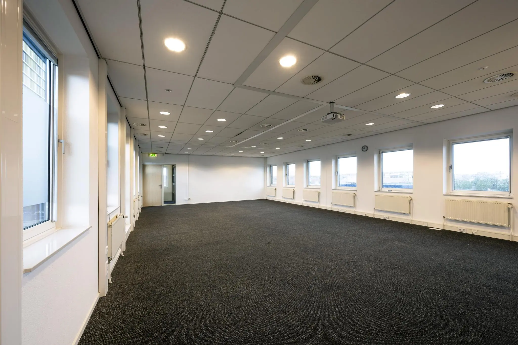 Lichte, lege kantoorruimte aan de Paasheuvelweg met ramen langs de muur en systeemplafond.