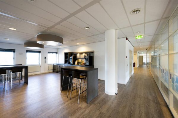 Moderne kantoorpantry aan de Paasheuvelweg met zitplekken, koffieapparaat en houten vloer.