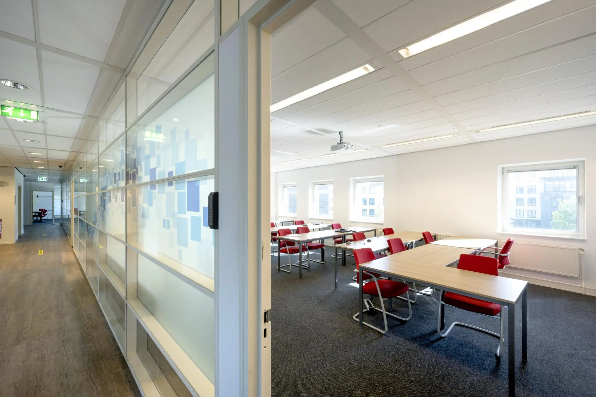 Licht en modern leslokaal aan de Paasheuvelweg met rode stoelen, houten tafels en grote ramen.