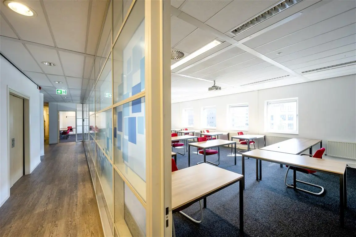 Lichte en moderne vergaderruimte met losse tafels en rode stoelen aan de Paasheuvelweg.