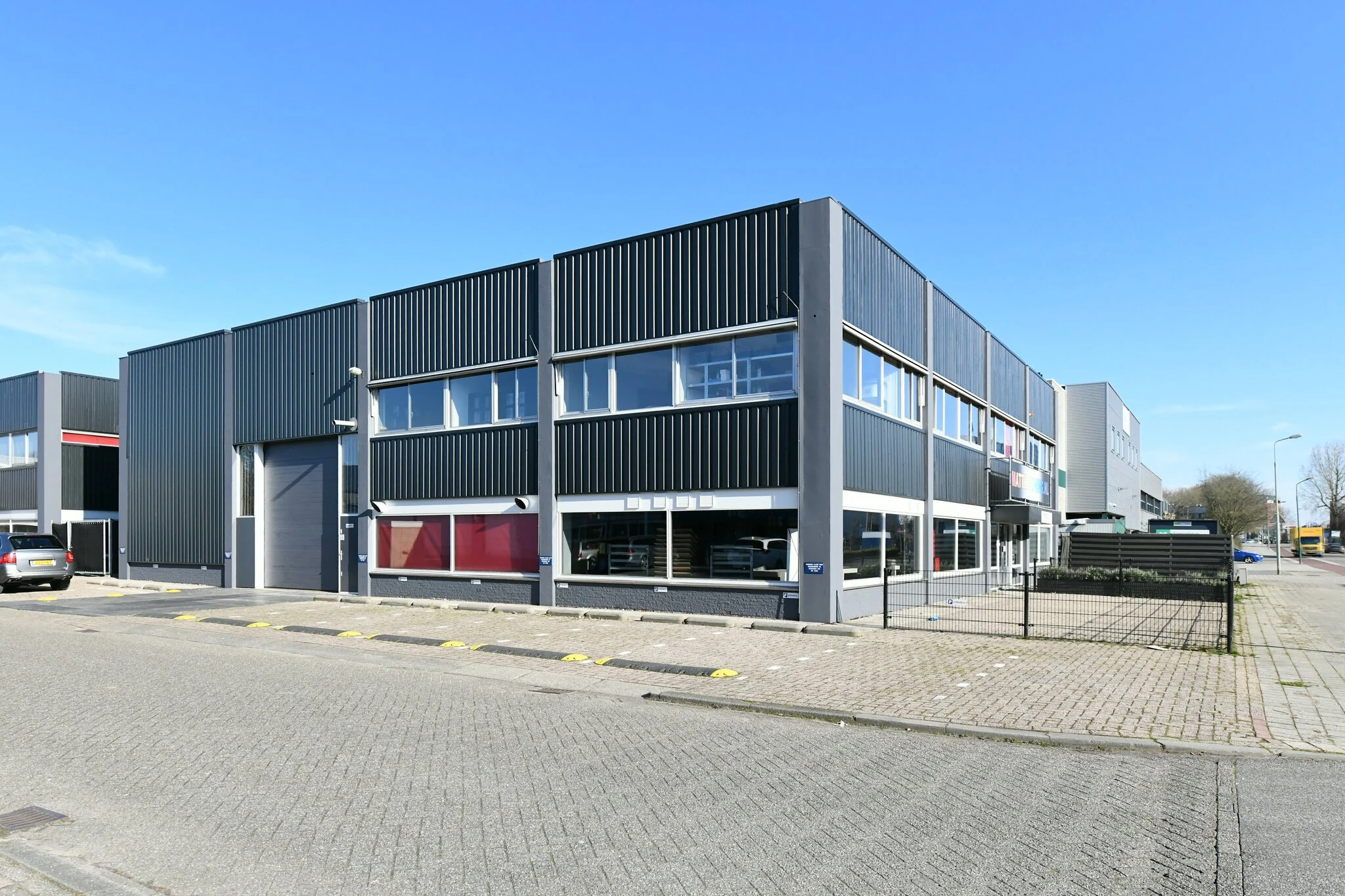 Modern bedrijfspand aan de Zonnebaan met zwart stalen gevelbekleding op een zonnige dag.