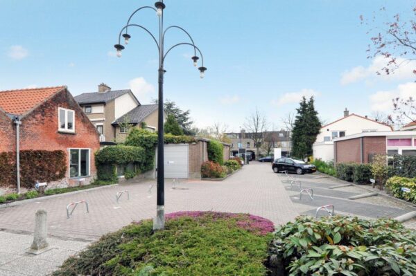 Straatbeeld van het Oosteinde met een open parkeerterrein, woonhuizen en een hoge lantaarnpaal in het midden.