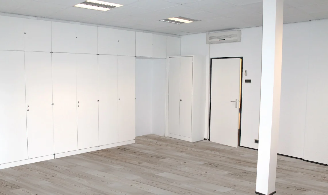 Lichte kamer met witte inbouwkasten, een witte deur en een licht houten vloer in een pand aan het Oosteinde.