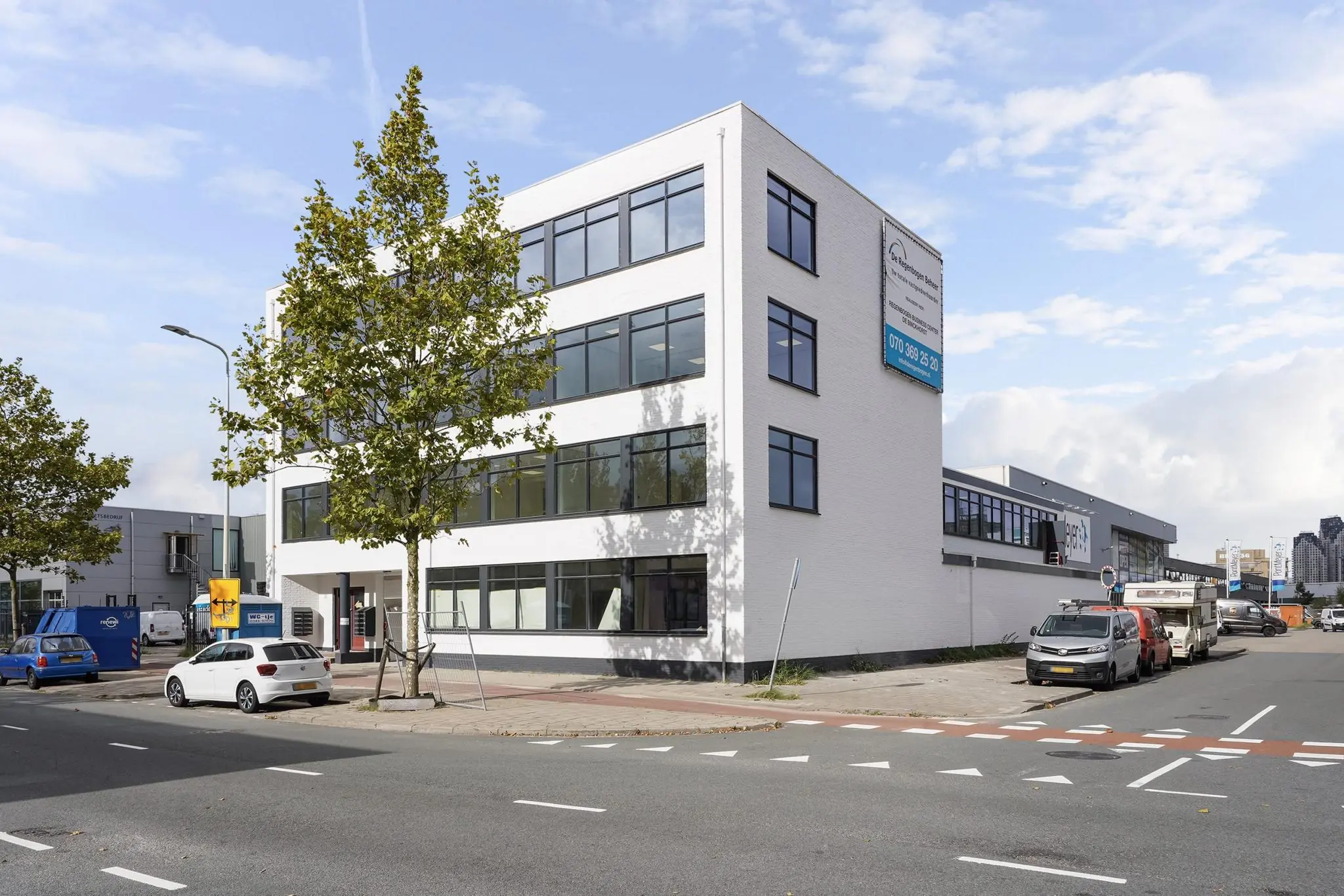 Wit kantoorgebouw aan de Mercuriusweg met grote ramen en geparkeerde auto's langs de straat.