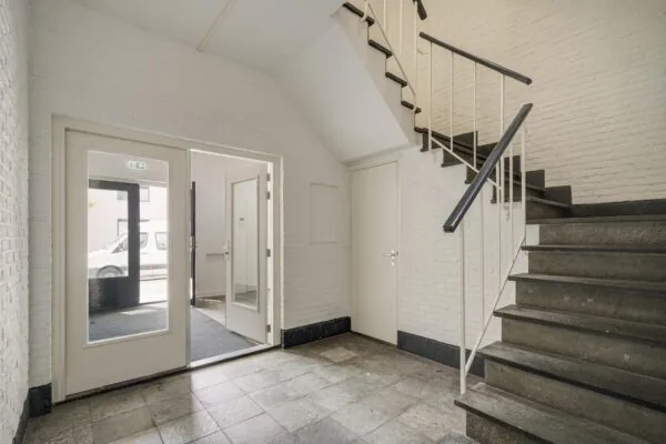 Entreehal van een gebouw aan de Mercuriusweg met stenen trap, witte muren en dubbele glazen deur naar buiten.