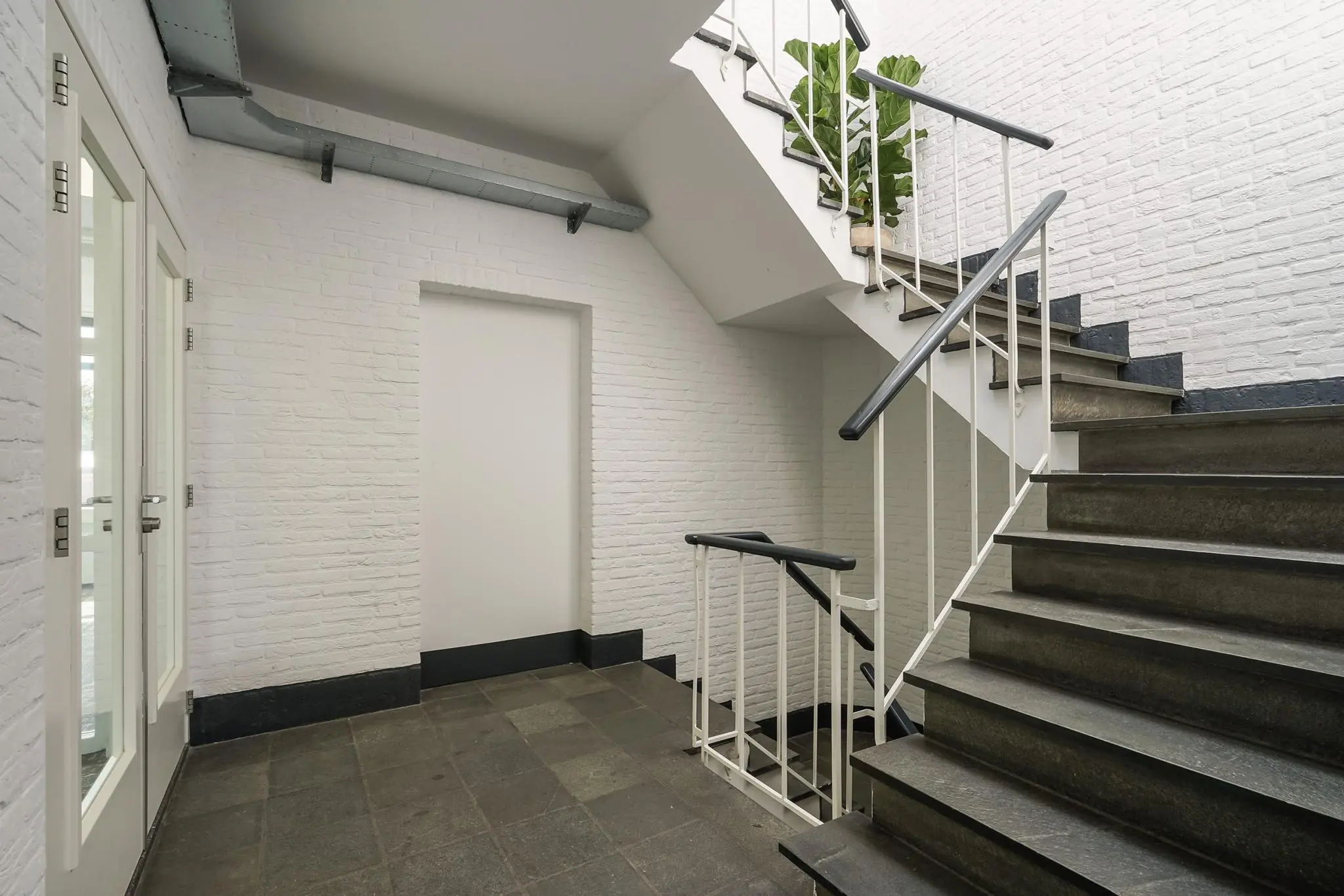 Trappenhuis met witte bakstenen muren, zwarte stenen treden en een plant op de overloop aan de Mercuriusweg.